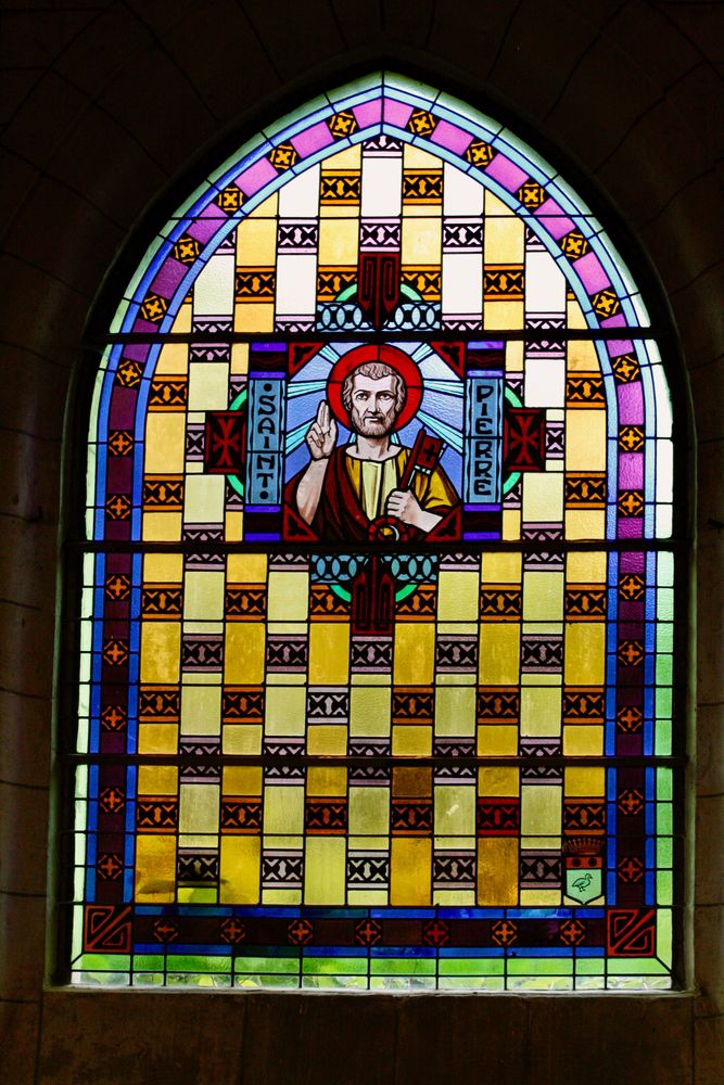 un vitrail coloré représentant Saint Pierre avec une auréole rouge et un livre à la main
